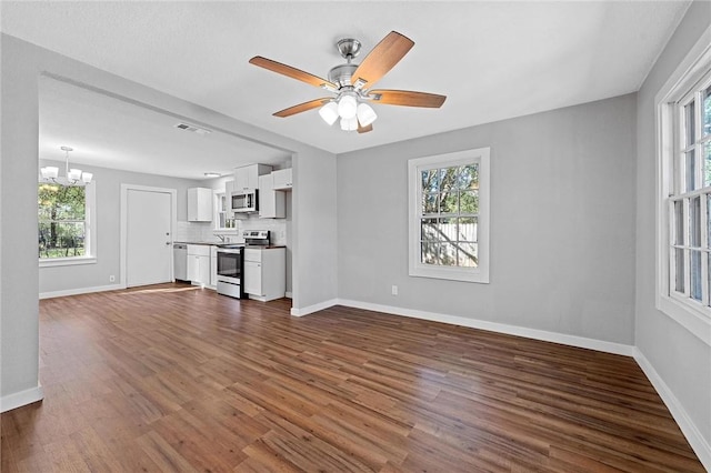 unfurnished living room with dark wood-type flooring and ceiling fan with notable chandelier