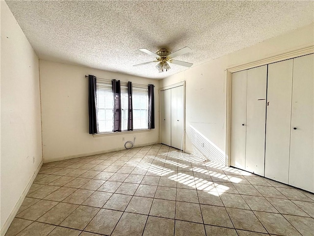 unfurnished bedroom featuring a textured ceiling, two closets, ceiling fan, and light tile patterned floors