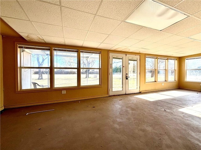 empty room with a drop ceiling, french doors, and concrete flooring