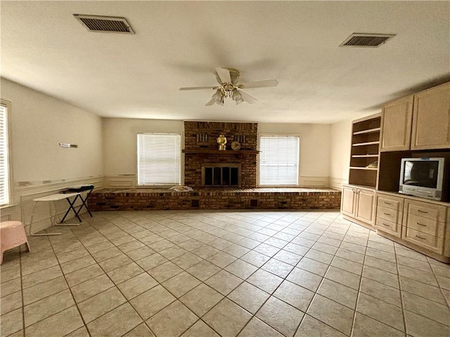 unfurnished living room featuring a fireplace, brick wall, light tile patterned flooring, and ceiling fan