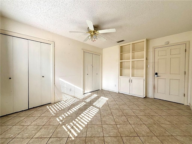 unfurnished bedroom featuring ceiling fan, multiple closets, light tile patterned flooring, and a textured ceiling