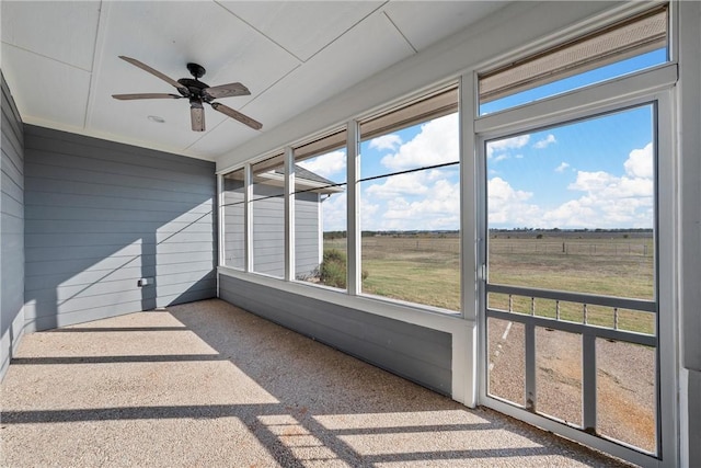 unfurnished sunroom featuring ceiling fan and a rural view