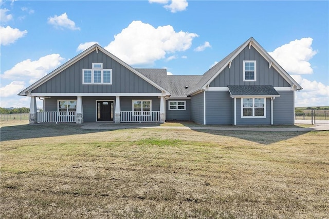 view of front of home featuring board and batten siding, a front yard, covered porch, and roof with shingles