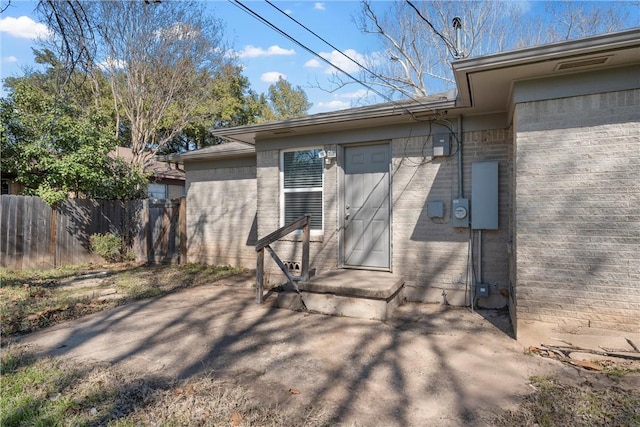 view of exterior entry featuring fence and brick siding