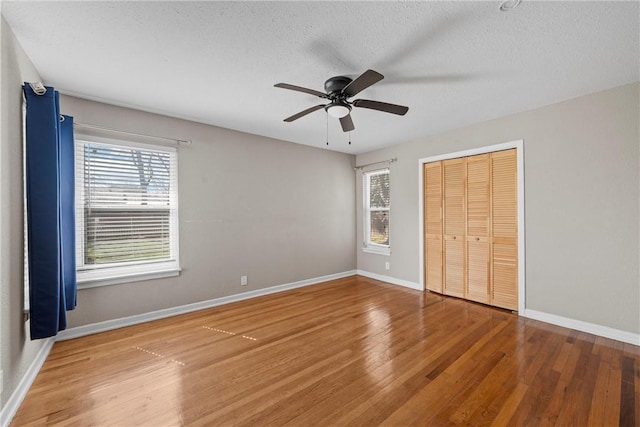 unfurnished bedroom with a closet, a textured ceiling, baseboards, and wood finished floors