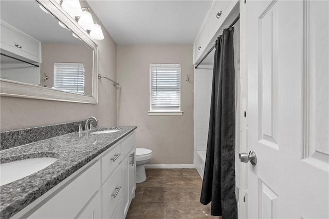 bathroom featuring double vanity, a sink, toilet, and baseboards