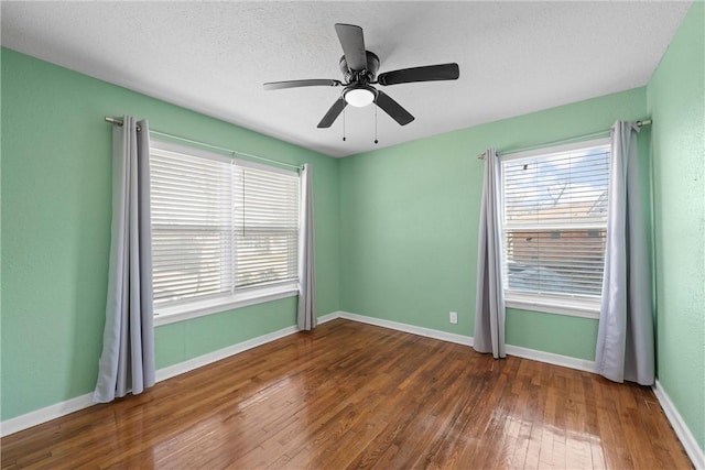 empty room with a ceiling fan, wood-type flooring, a textured ceiling, and baseboards