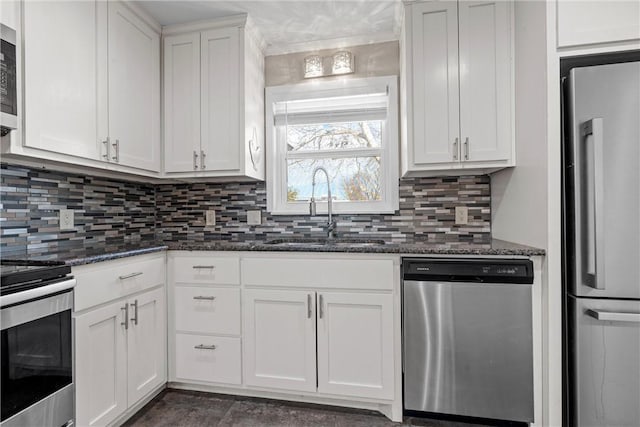 kitchen featuring stainless steel appliances, backsplash, white cabinets, a sink, and dark stone counters