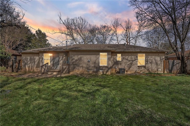 rear view of house featuring central AC, brick siding, a lawn, and fence