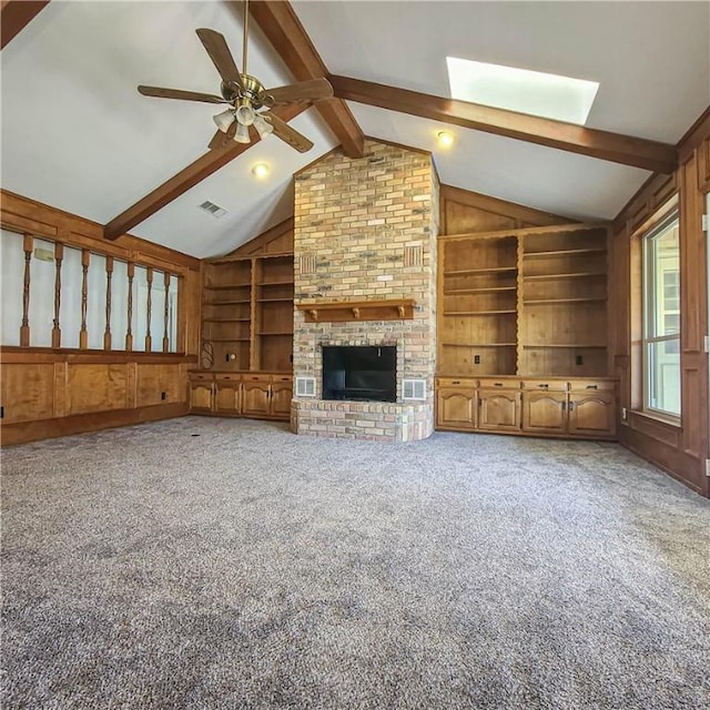 unfurnished living room featuring vaulted ceiling with skylight, carpet, ceiling fan, built in features, and a brick fireplace