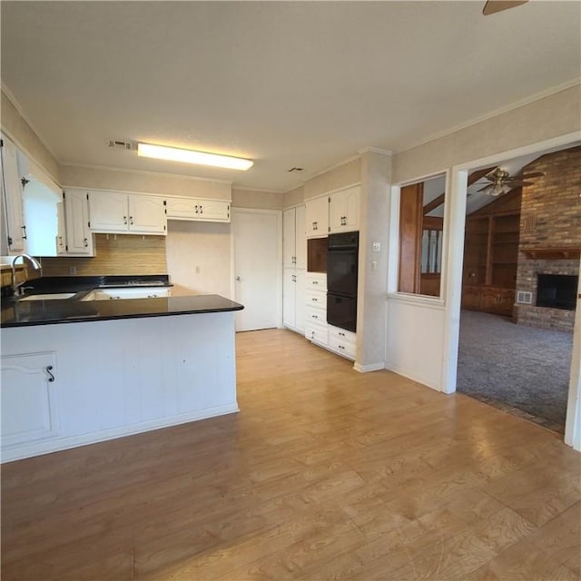 kitchen with white cabinets, double oven, a brick fireplace, sink, and ceiling fan