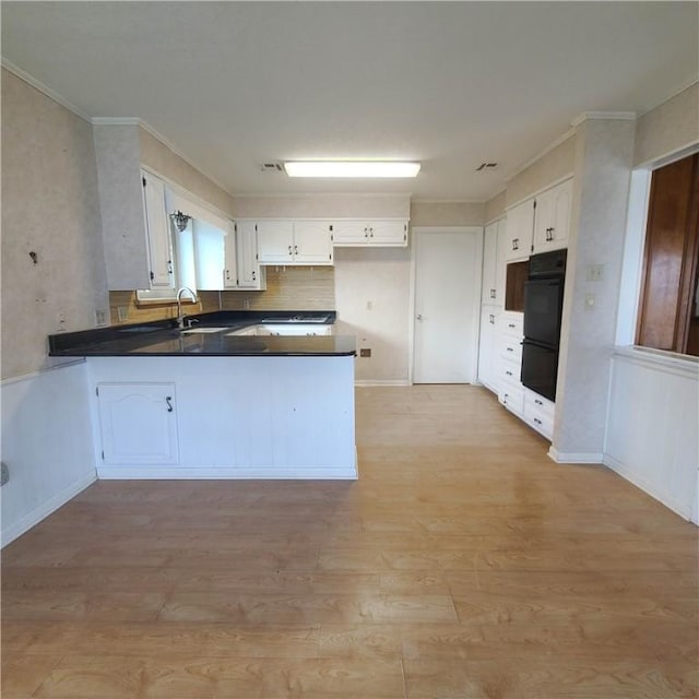 kitchen with black double oven, white cabinets, light wood-type flooring, sink, and kitchen peninsula