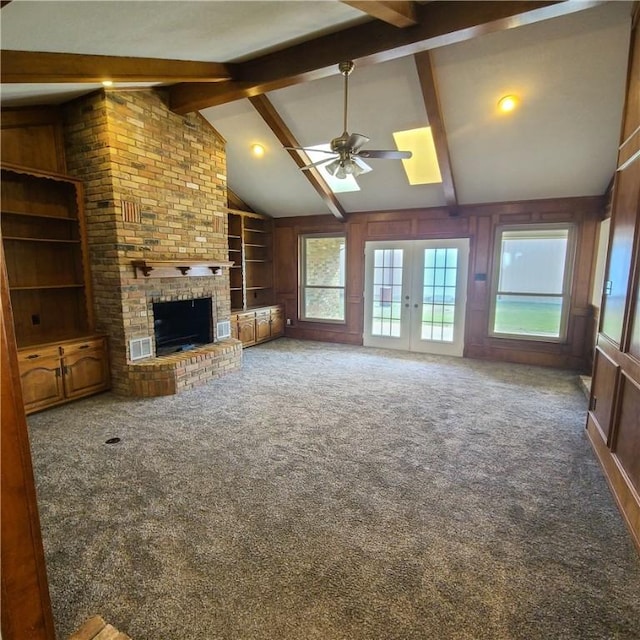 unfurnished living room featuring french doors, lofted ceiling with beams, carpet, a fireplace, and wooden walls