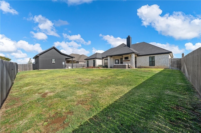 rear view of property featuring a yard, a chimney, stone siding, and a fenced backyard