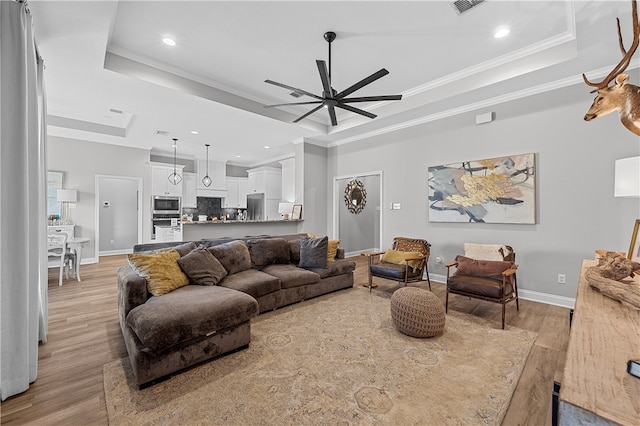 living room with light wood-type flooring, baseboards, a tray ceiling, and ornamental molding