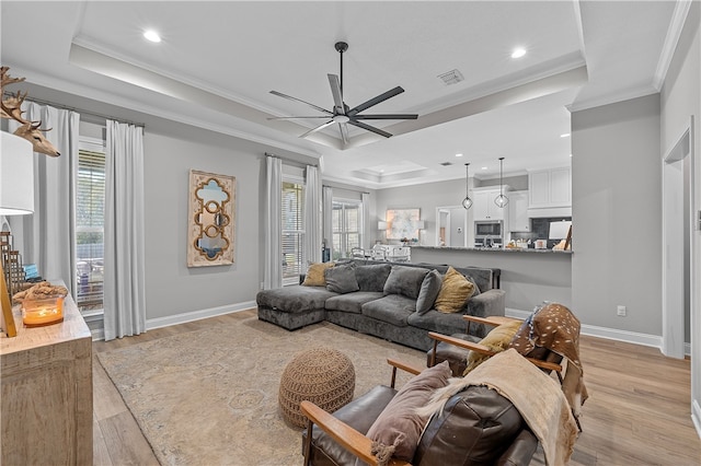 living area featuring light wood-style flooring, a raised ceiling, visible vents, and crown molding