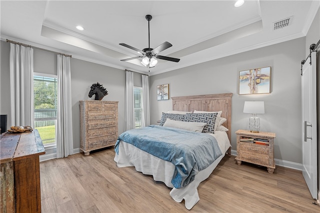 bedroom featuring light wood-type flooring, a raised ceiling, visible vents, and a barn door