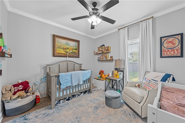 bedroom with ornamental molding, a nursery area, wood finished floors, and a ceiling fan