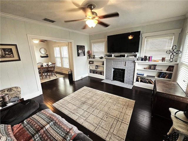 living room with dark wood-style floors, visible vents, crown molding, and a ceiling fan