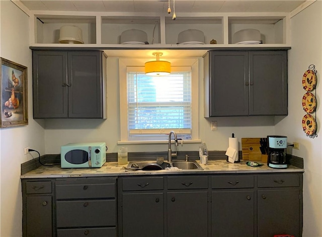 kitchen featuring white microwave, open shelves, gray cabinets, a sink, and light countertops