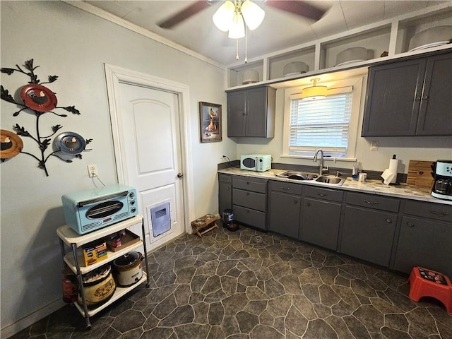 kitchen featuring a ceiling fan, gray cabinets, a sink, stone finish floor, and crown molding