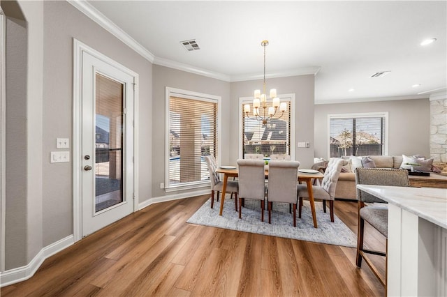 dining space with wood-type flooring, ornamental molding, and a notable chandelier