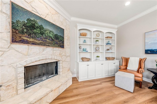 sitting room with crown molding, a stone fireplace, and light hardwood / wood-style flooring