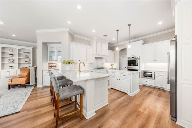 kitchen featuring decorative light fixtures, white cabinets, and a center island with sink