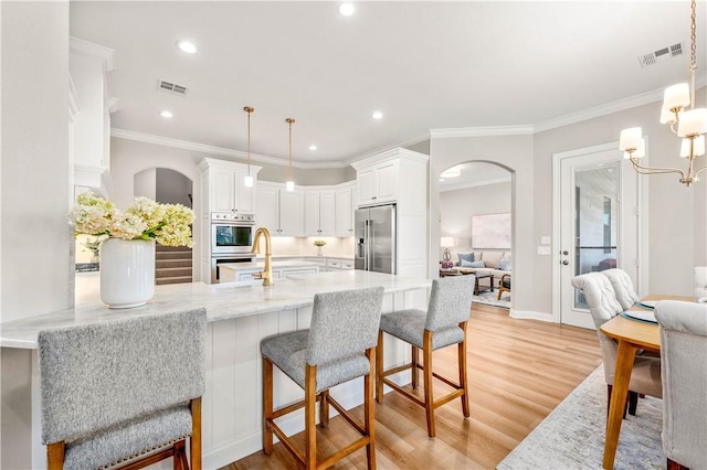 kitchen with kitchen peninsula, stainless steel appliances, white cabinets, and decorative light fixtures