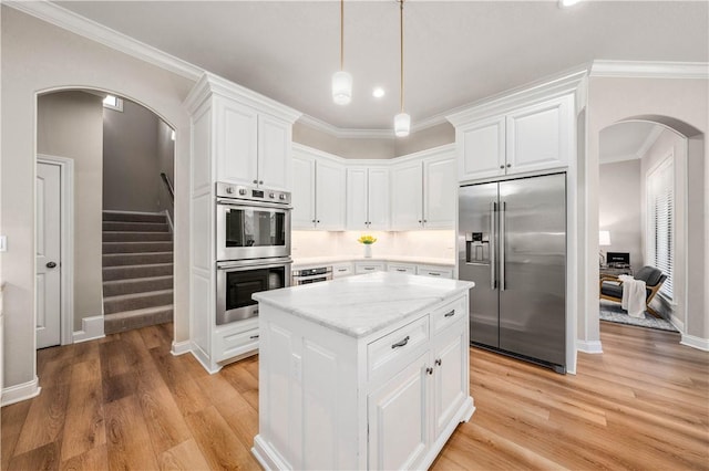 kitchen with white cabinetry, stainless steel appliances, hanging light fixtures, light stone countertops, and a kitchen island