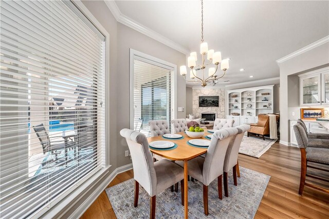 dining area featuring a fireplace, ornamental molding, a chandelier, and hardwood / wood-style floors