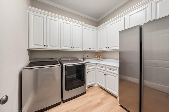 clothes washing area with washing machine and dryer, cabinets, sink, ornamental molding, and light hardwood / wood-style flooring