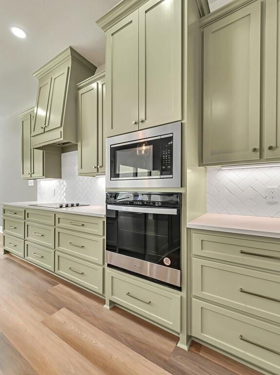 kitchen featuring appliances with stainless steel finishes, light wood-type flooring, tasteful backsplash, custom range hood, and green cabinetry