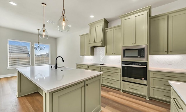 kitchen with appliances with stainless steel finishes, sink, decorative light fixtures, a center island with sink, and green cabinetry