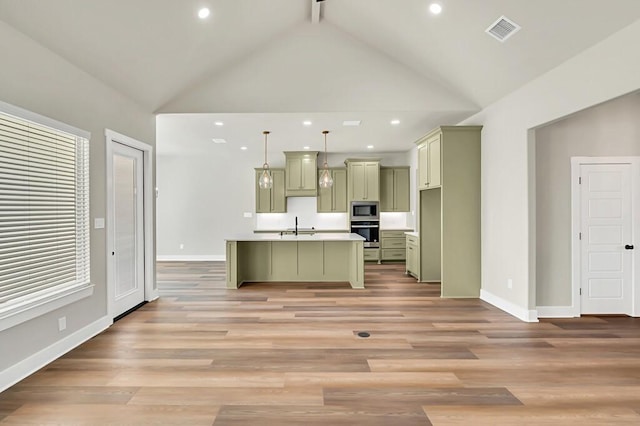 kitchen with pendant lighting, light wood-type flooring, appliances with stainless steel finishes, and an island with sink