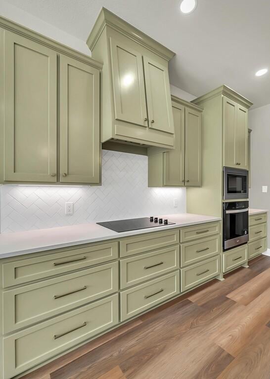 kitchen with appliances with stainless steel finishes, backsplash, green cabinetry, and wood-type flooring