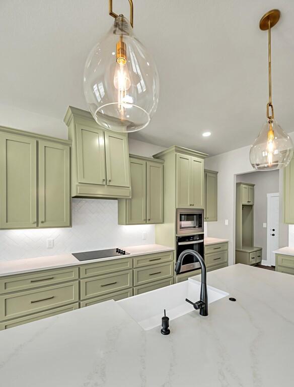 kitchen with pendant lighting, green cabinets, light stone countertops, and appliances with stainless steel finishes