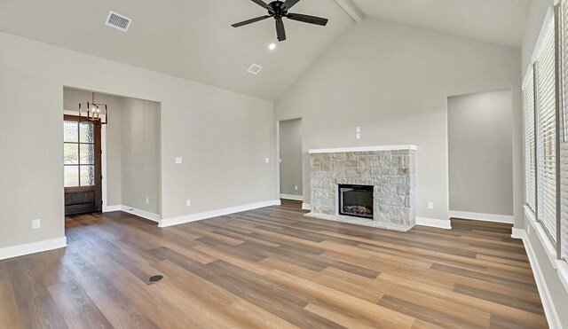 unfurnished living room featuring high vaulted ceiling, ceiling fan with notable chandelier, a stone fireplace, beamed ceiling, and wood-type flooring