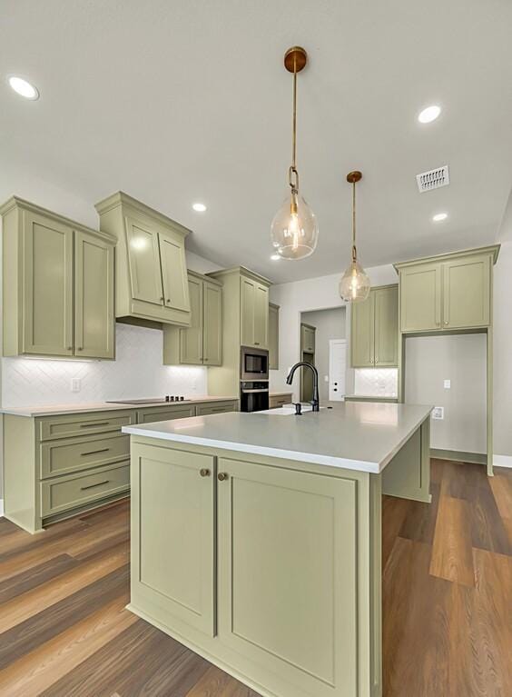 kitchen featuring pendant lighting, stainless steel microwave, dark wood-type flooring, oven, and an island with sink