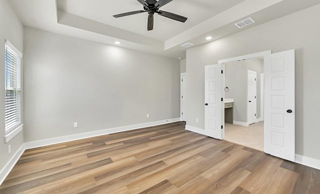 unfurnished bedroom with hardwood / wood-style floors, ceiling fan, and a tray ceiling