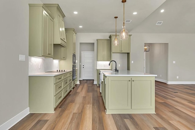 kitchen featuring a kitchen island with sink, hardwood / wood-style floors, pendant lighting, decorative backsplash, and green cabinetry