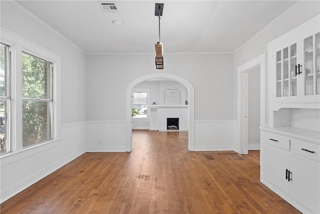 unfurnished dining area featuring a brick fireplace, ornamental molding, and hardwood / wood-style flooring