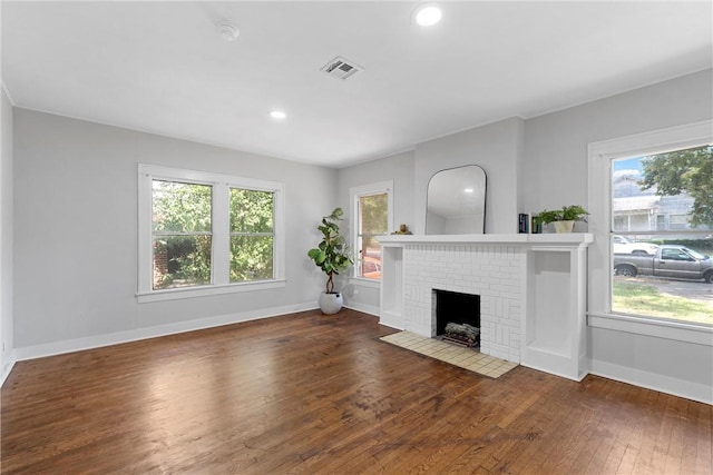 unfurnished living room featuring dark hardwood / wood-style floors, a brick fireplace, and a healthy amount of sunlight