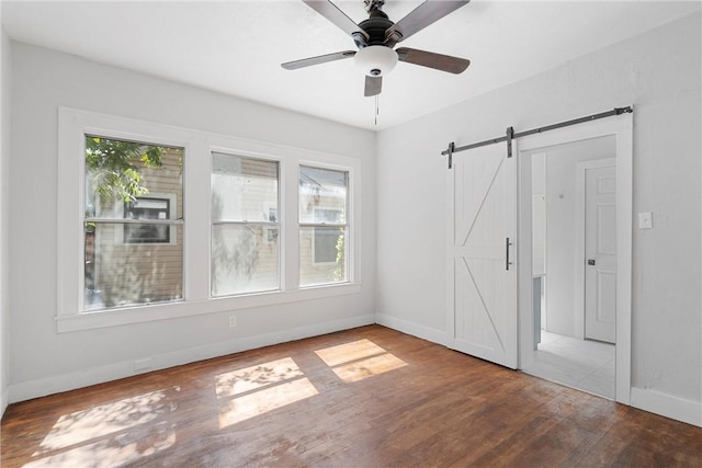 unfurnished room featuring wood-type flooring, a barn door, a wealth of natural light, and ceiling fan