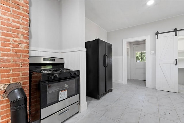 kitchen featuring black refrigerator, a barn door, brick wall, and stainless steel range with gas stovetop