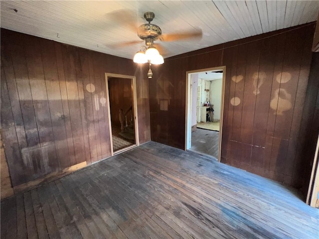 empty room featuring ceiling fan, dark hardwood / wood-style flooring, and wooden walls