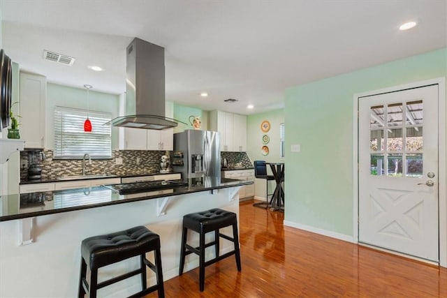 kitchen featuring island exhaust hood, a breakfast bar, sink, white cabinets, and stainless steel fridge with ice dispenser