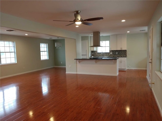 kitchen with decorative backsplash, a kitchen breakfast bar, ceiling fan with notable chandelier, white cabinetry, and range hood