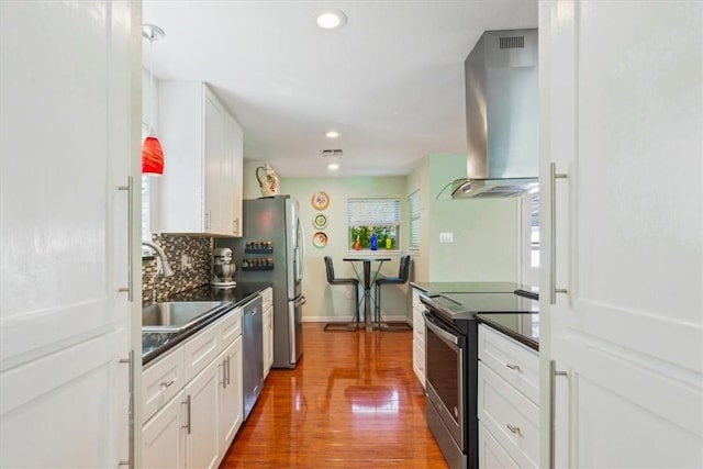 kitchen with tasteful backsplash, stainless steel appliances, sink, wall chimney range hood, and white cabinetry