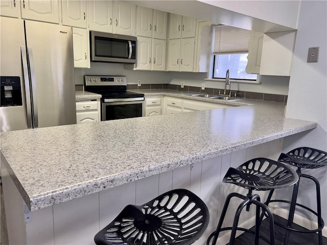 kitchen with white cabinetry, sink, kitchen peninsula, a breakfast bar, and appliances with stainless steel finishes